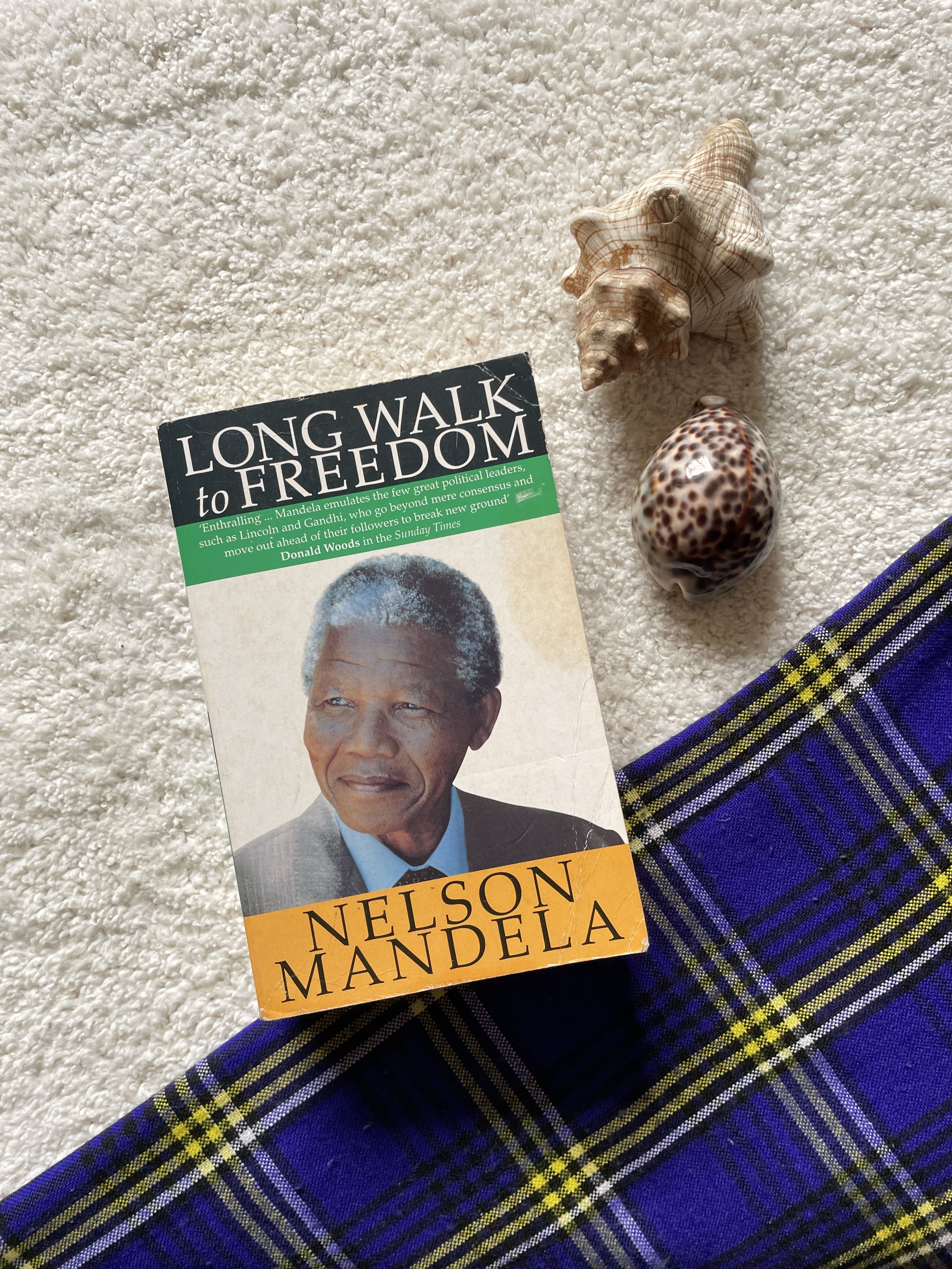 Book titled 'Long Walk to Freedom' by Nelson Mandela on a textured surface with shells.
