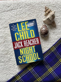 Book titled 'Night School' by Lee Child and Jack Reacher on a textured surface with shells and fabric.